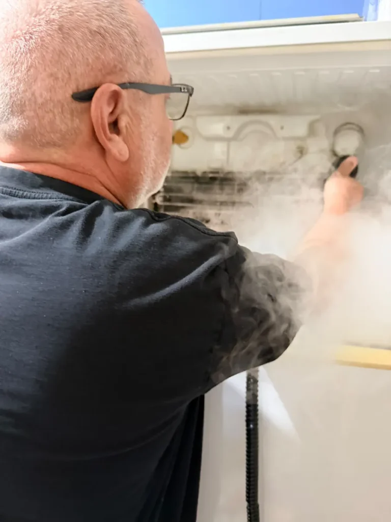 Appliance technician using a steam cleaner to remove mould from inside a refrigerator